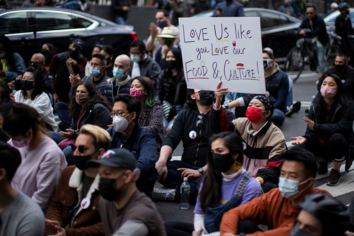 Asyalı bir kadının öldürüldüğü binanın önündeki oturma eyleminde başka bir karede, afişte, 'Mutfağımızı ve kültürümüzü sevdiğiniz gibi bizi de sevin' ifadesi yer alıyor.