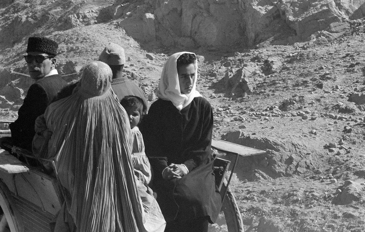 Kasım, 1959’da geleneksel kıyafetler içinde Afgan kadınlar, erkekler ve çocuklar; çorak, taşlı bir yolda at arabasının arkasında seyahat ederken görülüyor.