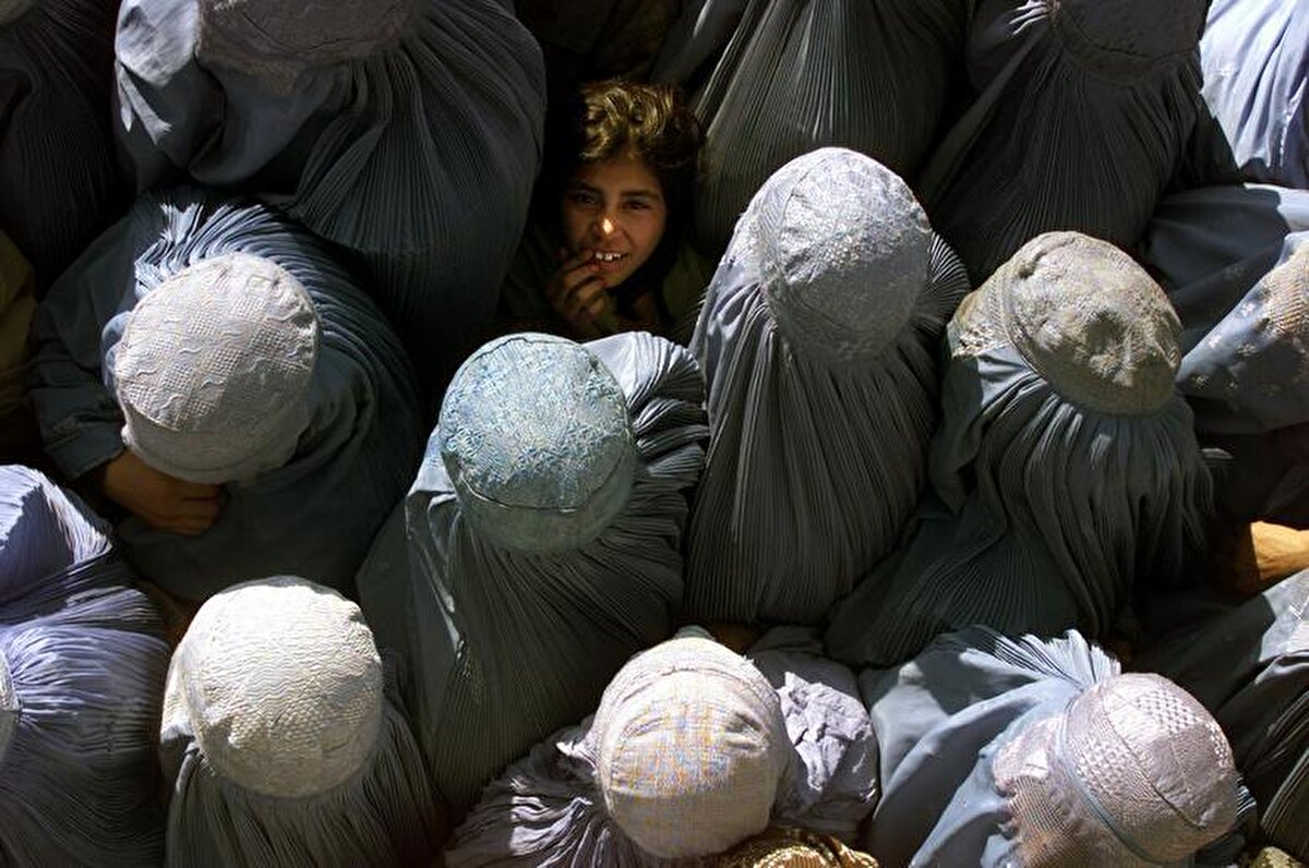 Kabil'de bir gıda dağıtım merkezinin önünde sıra bekleyen Afgan kadınlar ve gökyüzüne doğru bakan bir kız çocuğu. 7 Aralık, 2001.