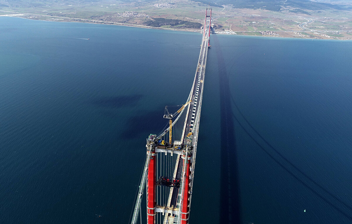 Ana kablo imalatları kapsamında orta açıklıklarda 288, yan açıklıklarda ilave 16 kablo demeti ile toplam 304 kablo demetinden oluşan ana kablo montajı ile tabliyeleri ana kabloya bağlayan kelepçe ve askı halatı montaj çalışmaları da sonlandı. Ana kabloyu dış etkilerden de koruyacak tel sargı çalışmaları sürüyor.<br><br>