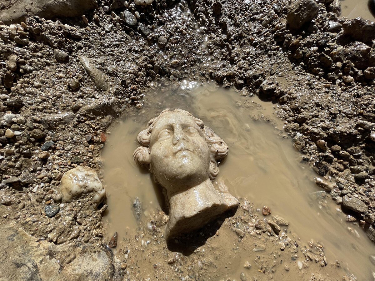 Son kazı çalışmalarında 2 metre 10 santim yüksekliğindeki erkek heykelini korumaya alan arkeologlar, Yunan mitolojisinde aşk tanrısı olarak bilinen 'Eros', şarap tanrısı 'Dionysos' ve yarı tanrı 'Herakles'in heykel başlarını gün yüzüne çıkardı.<br>Penkalas Çayı'ndaki kazılarda Roma dönemine ait 2 No'lu mermer köprünün restorasyonunun tamamlandığını kaydeden Kütahya Dumlupınar Üniversitesi Arkeoloji Bölümü'nde görevli, Kazı Başkanı Prof. Dr. Gökhan Coşkun, tamamen yıkılan 3 No'lu köprüde çalışmaların sürdüğünü söyledi. Her gün yeni esere ulaşıldığına dikkat çeken Coşkun, “2022 yılında köprünün bulunduğu alanda yaptığımız çalışmalarda bizi oldukça heyecanlandıran sürpriz buluntularla karşılaşmaya devam ettik.