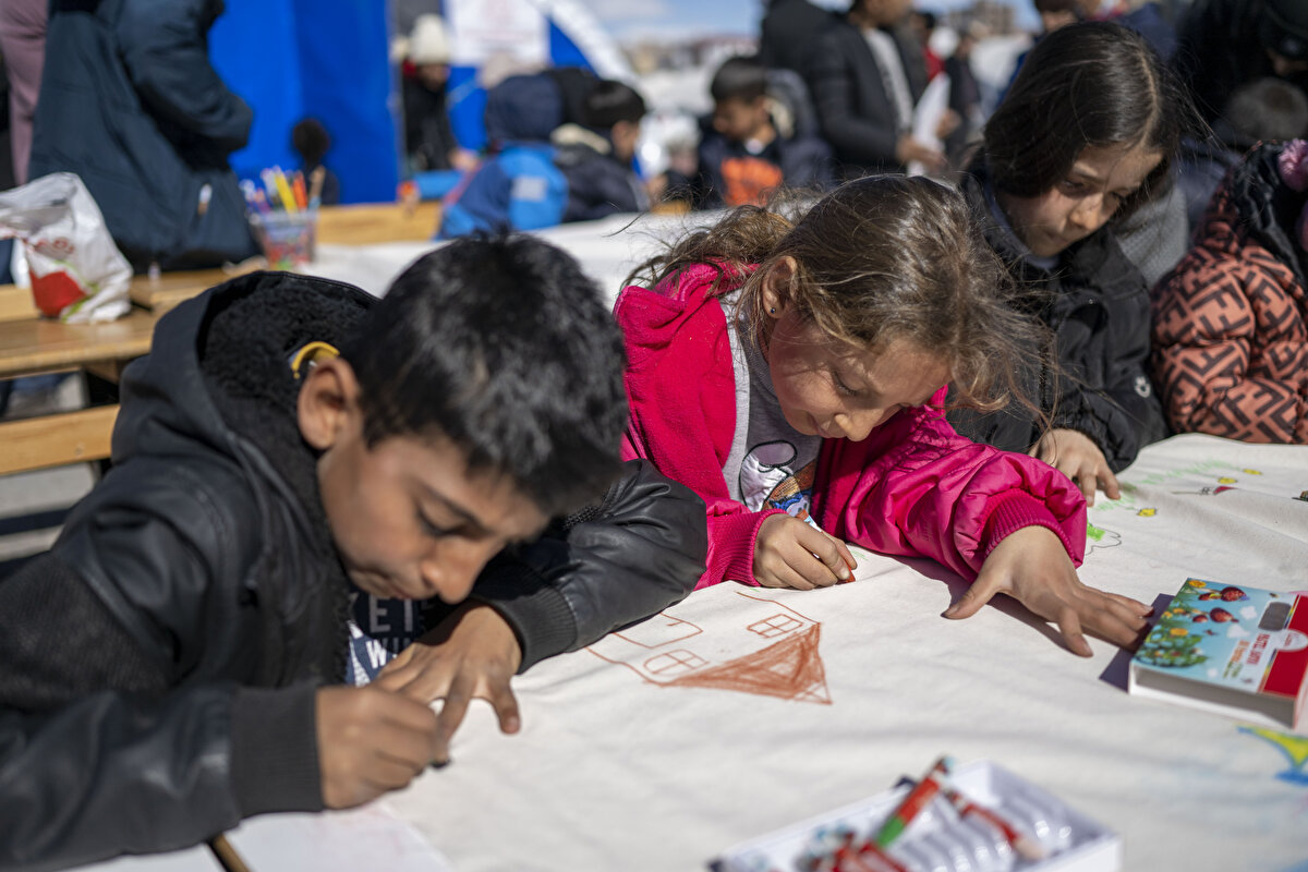 Yaklaşık 20 çocuk, öğretmenlerin getirdiği 5 metrekarelik bezin üzerine büyük bir köy resmi çizdi.<br>