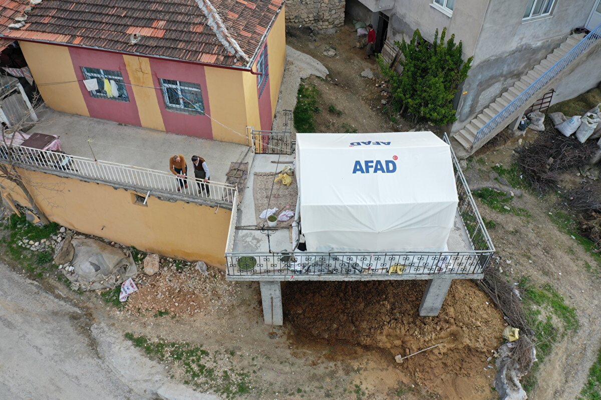 Depremlerde ahırları ağır, evleri ise az hasar alan Karacan çifti, Afet ve Acil Durum Yönetimi Başkanlığınca (AFAD) verilen çadırı, yakınlarının da yardımıyla iki yıl önce yaptıkları ve sadece dört kolonu bulunan tek katlı yapının üstüne yerleştirdi.<br>
