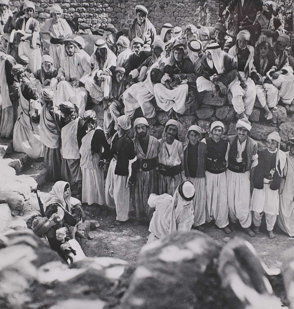 Laliş'te her yıl düzenlenen Yezîdî festivalinde Dabke dansını oynayan bir grup, Ekim 1946.<br><br>Dabke (bir çeşit halay); tek bir kişi tarafından yönetilen, uzun sıralı, kadınlı erkekli gruplar halinde oynanan danslardır. Bu görüntüde, önde bir müzisyenin bulunduğu çıplak ayaklı geleneksel kıyafetler giyen dansçılar, el ele tutuşup merdivenlerden çıkmaktadır.