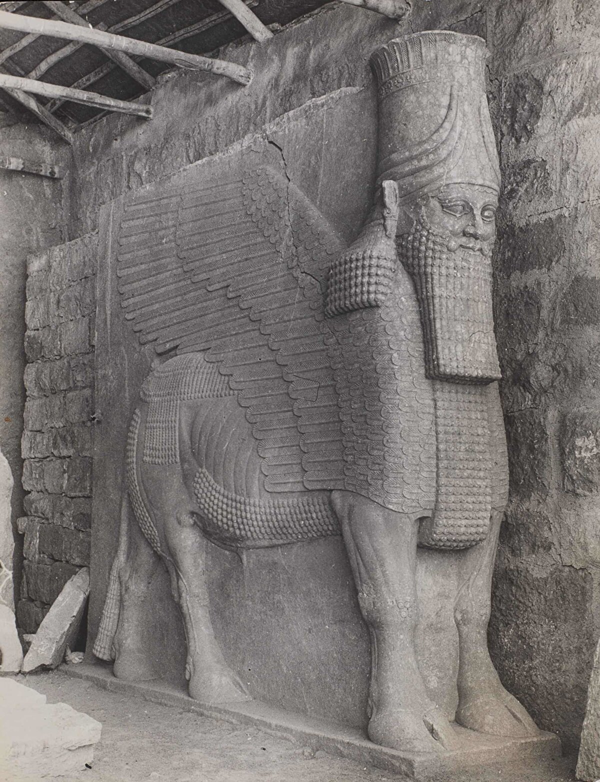 Musul'un hemen dışında Ninova'nın kanatlı aslanlarından biri, Ağustos 1944.<br><br>Bu oyulmuş figür, insan başlı, kartal kanatlı ve boğa gövdeli bir yaratık olan Lamassu olarak bilinir. Yaklaşık 2700 yıl önce, Asur Kralı Sennacherib'in saltanatı sırasında Ninova'ya giden ana kapıyı korumak için yapılan bu devasa heykel, 1941 yılının Nisan ayında yağan şiddetli yağmur sayesinde Kuzey Şehir Kapısı'nda aniden belirmiştir. Yüzyılların tahrip edemediği figür, 2015 yılında IŞİD tarafından imha edilmiştir.