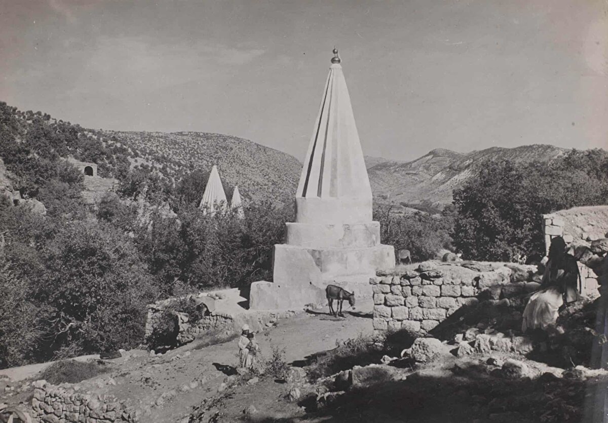 Yezîdî Şeyh Adî Türbesi’nin kuleleri, Ağustos 1944.<br><br>Bu fotoğraf, Musul'un kuzeyindeki bir dağ vadisi olan Laleş'teki en önemli yapı olan Şeyh Adî b. Müsâfir'in mezarını göstermektedir. Kulelerin şekli, Yezîdî ibadetinde güneşin önemini yansıtmaktadır.<br><br>Zerdüştîlik, Maniheizm, Mitraizm, Yahudilik ve Hristiyanlık’tan, ayrıca İslâm ve tasavvuftan büyük ölçüde etkilenen Yezîdîlerin kendi içlerine dönük yaşantılarından dolayı inanç ve ibadet esaslarının tam olarak belirlenmesi mümkün olmamıştır. Yezîdî inancının merkezinde Tanrı ile birlikte O’nun yarattığı yedi melek ve bu melekleri idare eden Melek Tâvus bulunmaktadır. Yezîdîler, meleklerin zaman zaman yere indiklerine, dünyanın düzenini sağlayacak kutsal metinler ve kurallar getirdiklerine, kendilerine vekâlet edecek şeyhler bıraktıktan sonra cennete çekildiklerine inanmaktadır.