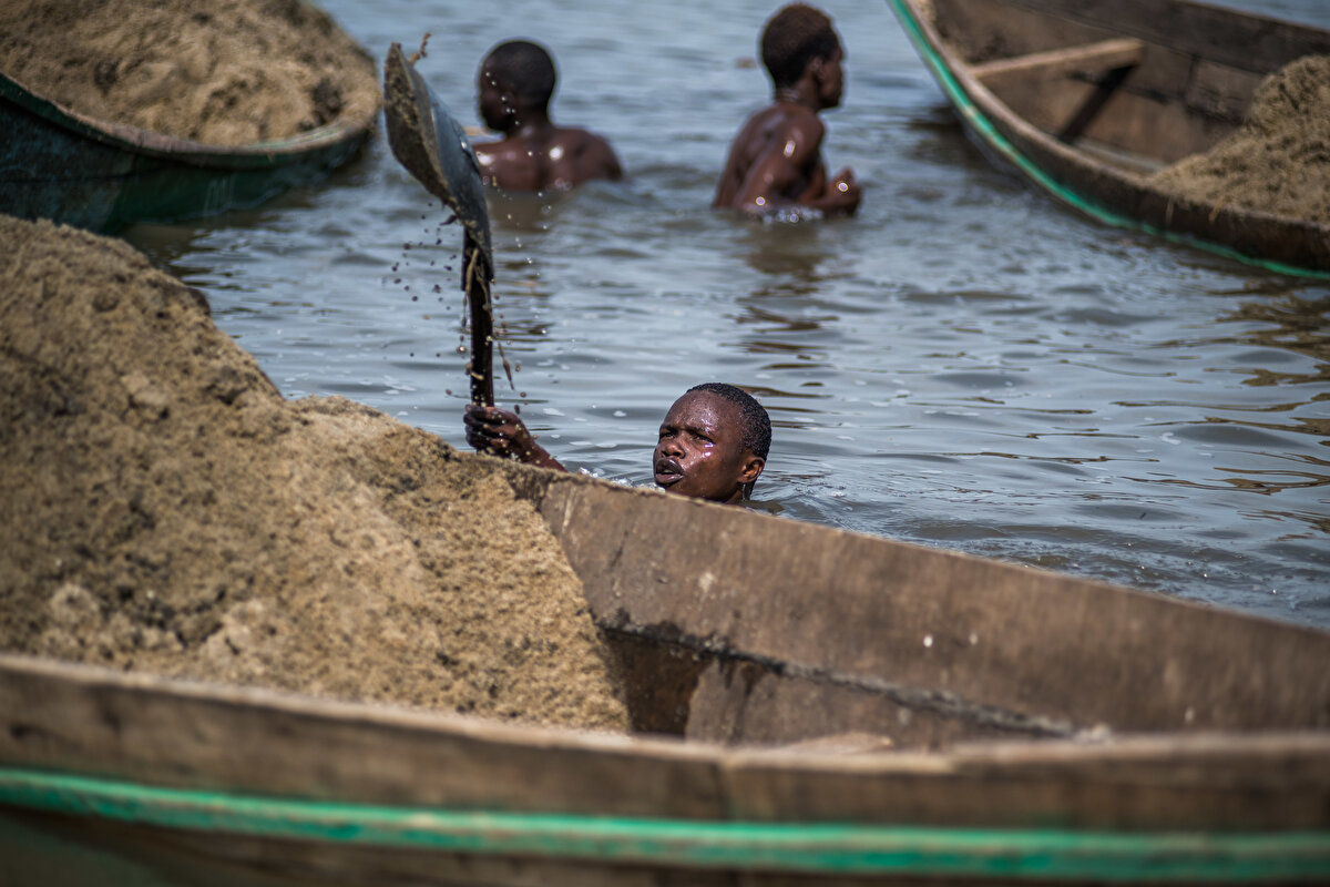 Köylü işçiler, ellerindeki küreklerle gölün dibinden çıkardıkları kumları tekneleriyle kıyıya taşıyor.
