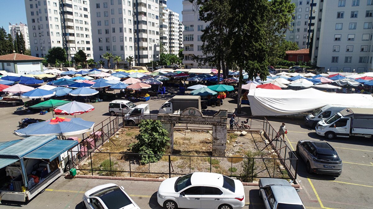 Pazarcıların açtığı şemsiyelerin, park eden araçların arasında kalan ve yakın zamanda etrafı çitlerle çevrilen kapının etrafında ise çöpler ve yabani otlar bulunuyor.<br>