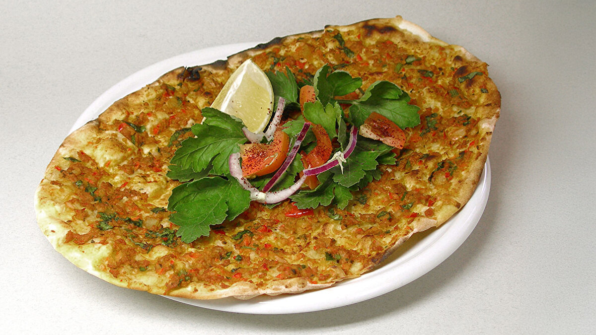 Lahmacun<br><br><br>Arapça lahm (et) + acim (yoğrulmuş) → “Yoğrulmuş et.”<br><br>Hamur üzerine yayılan kıymalı yemek