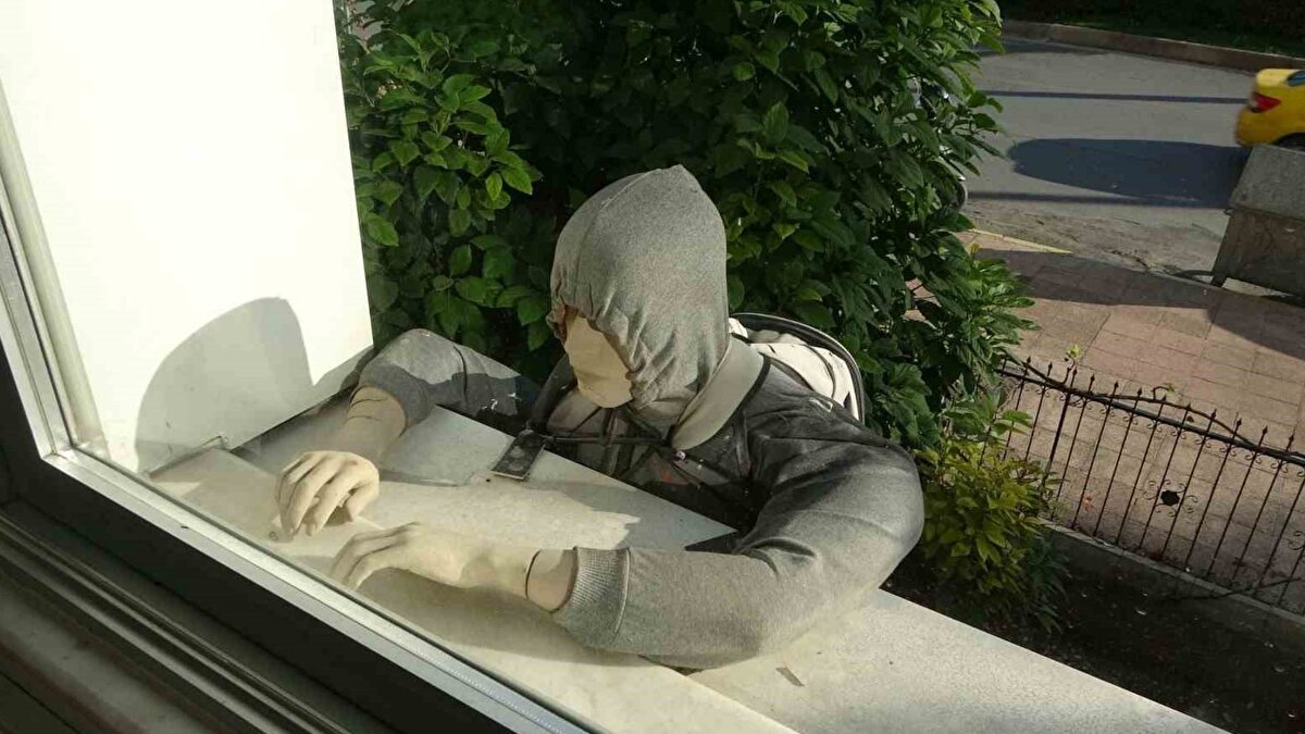 Mersin’de, sıradan bir işyeri hırsızlık riskine dikkat çekmek için ilginç bir yönteme başvurdu. Merkez Yenişehir ilçesi Cumhuriyet Mahallesi’nde bulunan bir sigorta firması, yaklaşık beş yıl önce binanın birinci kat penceresine, kapüşonlu ve sırt çantalı bir cansız manken yerleştirdi. Bu mankenin amacı, bölge halkını ev ve işyeri sigortası yaptırmaya teşvik ederek hırsızlık olaylarına karşı uyanık olmaya çağırmaktı.