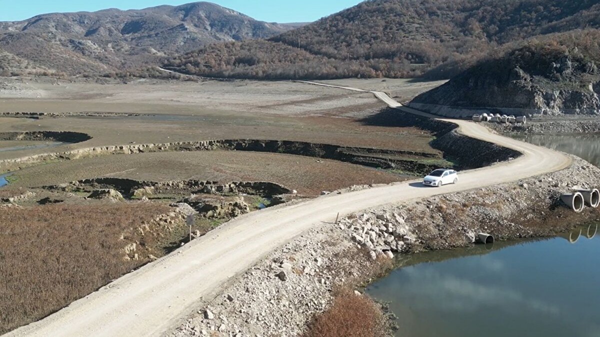 Kırsal ulaşımı kısaltacak yeni güzergâh<br><br>Bölgedeki köy muhtarlarının 2022 yılında ortak taleple başlattığı süreç, baraj suyunun çekildiği zamanlarda yoğun kullanılan kısa yolun resmi olarak projelendirilmesiyle sonuçlandı. Mevcut virajlı rotaya kıyasla mesafeyi yaklaşık 18 kilometreden 500 metreye kadar düşüren güzergâh, yıllardır bölge halkına ciddi zaman ve yakıt tasarrufu sağlıyordu. Ancak yolun yalnızca belirli dönemlerde kullanılabiliyor olması, güvenli bir çözüm ihtiyacını artırmıştı.