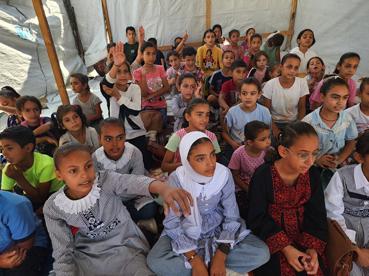 İsrail saldırısında evi yıkılan Gazzeli öğretmen, kurduğu çadır okulda öğrencilere ders veriyor İsrail ordusunun Gazze Şeridi'nin güneyindeki Han Yunus kentine düzenlediği saldırılarda evi yıkılan öğretmen Alaa Abu Mustafa, yıkılan evinin enkazı üzerine kurduğu çadır okulda öğrencilere ders vermeye devam ediyor. Öğretmen Alaa, kısıtlı ve zor şartlara rağmen ilkokul öğrencilerinin eğitimden mahrum kalmaması için çaba sarf ediyor. Foto MuhabiriHani Alshaer YayınlayanMustafa Cantürk