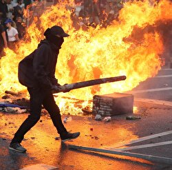 An anti-G20 protester stands in front of a burning street barricade 