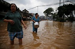 Women wade through a flooded street in Jatinegara district in Jakarta