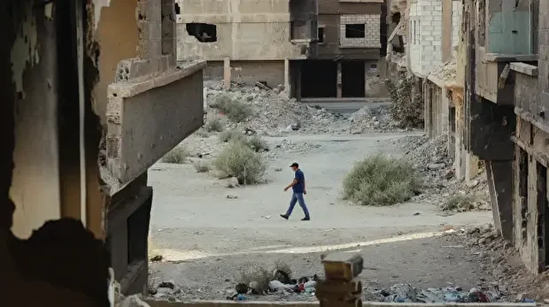Un homme marche dans une rue endommagée, encadrée par les vestiges de bâtiments détruits dans le camp de Yarmouk, à Damas, en Syrie, le 8 novembre 2025.