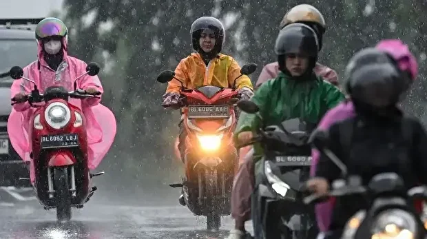 Des automobilistes vêtus d'imperméables roulent dans une rue sous la pluie à Banda Aceh en Indonésie, le 26 novembre 2025.
