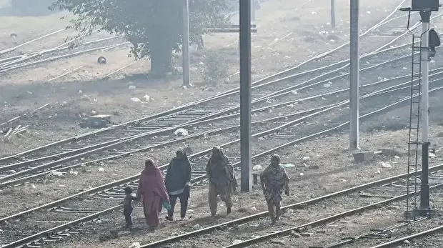 Des femmes accompagnées d'un enfant marchent le long d'une voie ferrée jonchée de détritus, dans un épais brouillard de pollution, à Lahore, le 1er décembre 2025.