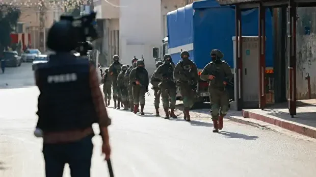 Un journaliste filme des soldats israéliens marchant dans une rue lors d'une opération à Qalqilyah, en Cisjordanie occupée, le 4 décembre 2025. 
