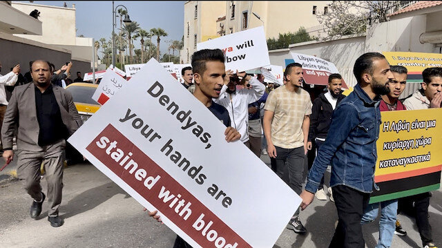 Libyalı bir protestocu elinde 'Dendias senin elinde kan lekesi var' yazılı bir pankart taşıyor.