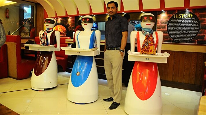 Osama Aziz poses for a photo with robot waitresses, which are built and developed by himself, at a local fast food restaurant in Multan, Pakistan on July 08, 2017.
