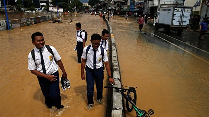 Students on their way to school wade through a flooded street in Jakarta