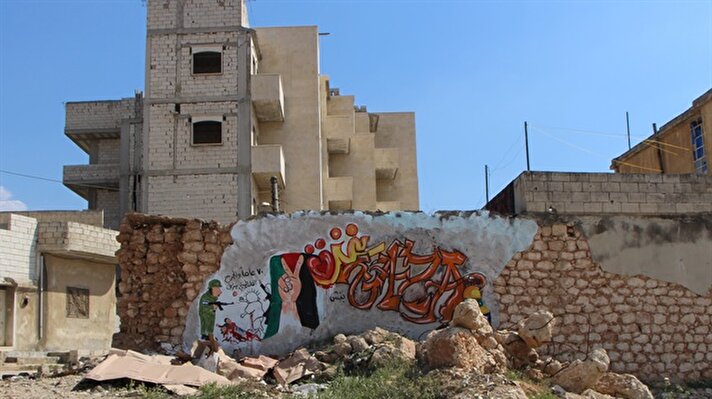  İdlib iline bağlı Binniş ilçesinde yaşayan 35 yaşındaki Aziz Esmer, Esed rejiminin hava saldırılarında yıkılan binaların duvarlarına bir yıldır Suriye'deki iç savaşı anlatan resimler çiziyor.
