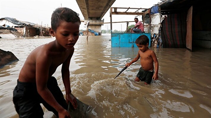 Children wade through flood waters as a man sits outside his submerged shanty