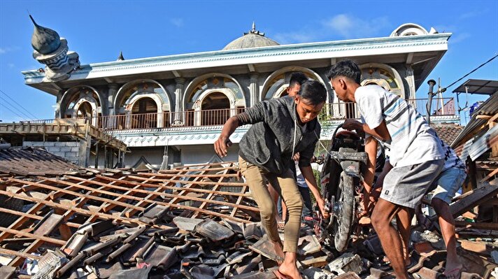 People recover a motorcycle from a damaged home near a mosque 