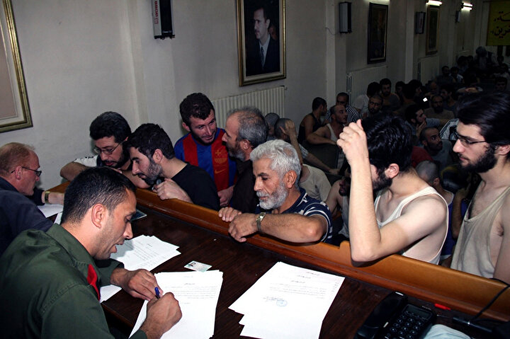 Suriyeli mahkûmlar 2012 yılında Şam Polis Kontrol Merkezi’nde serbest kalış belgelerini imzalarken. (Görsel: Bassem Tellawi / Associated Press)