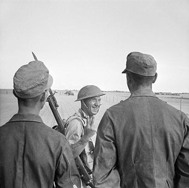 Bir İngiliz askeri el-Alemeyn’de esir alınan Alman tutsaklara zafer işareti yapıyor. (26 Ekim 1942)