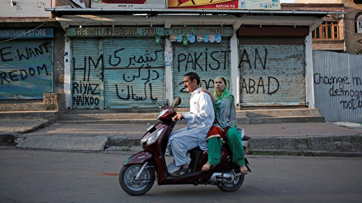 Keşmirli çift, Srinagar'daki kısıtlamalar sırasında üzeri grafitilerle dolan kapalı dükkanların önünden geçiyor.
