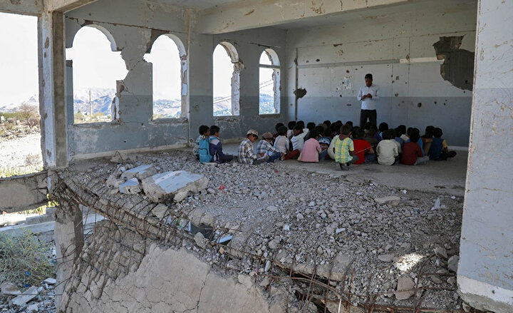 Yemenli çocuklar, yeni akademik yılın ilk gününde, öğretmenlerini, hava saldırılarında ağır hasar gören bir sınıfta dinliyorlar.