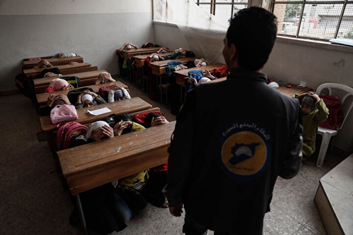 Şam’ın kuzeydoğusunda bulunan Harasta’da sivil savunma farkındalığı kazandırılması için düzenlenen kampanya kapsamında Beyaz Baretliler olarak da bilinen Suriye sivil savunma ekiplerinden bir görevli, hava saldırısıyla karşı karşıya kalmaları durumunda öğrencilere, kendilerini nasıl koruyacaklarını öğretiyor.