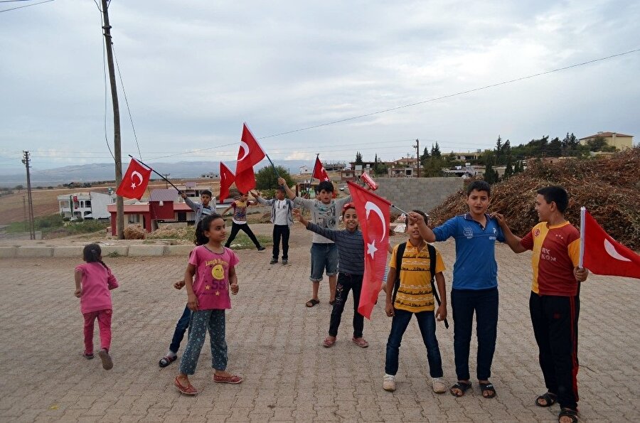 Sınır bölgesinde yer alan mahallelerde oyun oynayan çocuklar ellerinde Türk bayrağı taşıyor.