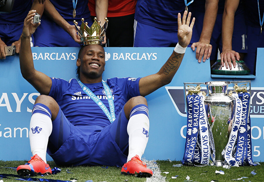 Chelsea formasıyla Premier Lig şampiyonluğu yaşayan Drogba, kupalarla ve taçla poz veriyor.