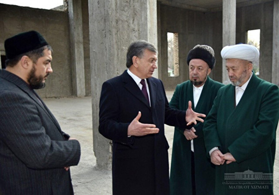 Cumhurbaşkanı Şevket Mirziyoyev Özbekistan Dini İdaresi Başkanı Osmanhan Alimov'la ( en sağda) 2015 yılında vefat eden eski Özbekistan Müftüsü Muhammed Sadık Muhammed Yusuf'un adını taşıyacak caminin yapılacağı mekanda konuşurken.