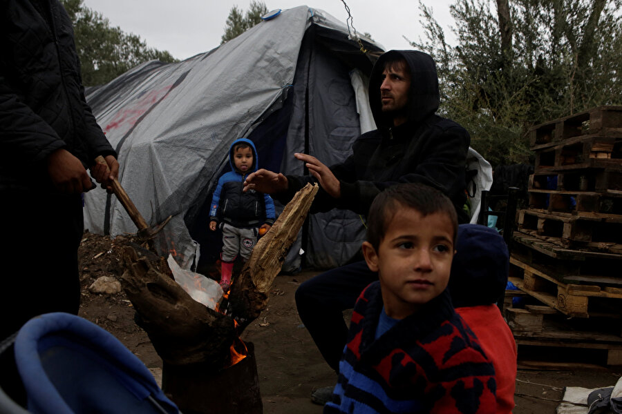 Çadırda yaşayan göçmen aile yaktıkları ateşte ısınmaya çalışıyor.