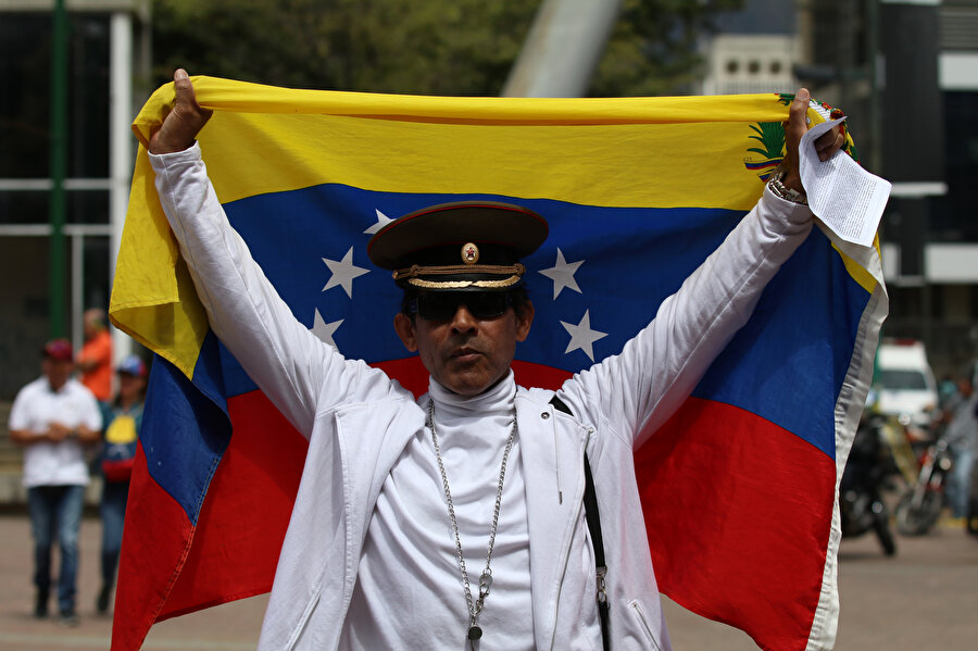 Ülkedeki gösterilerde bayrakla objektiflere bakan bir Venezuelalı.