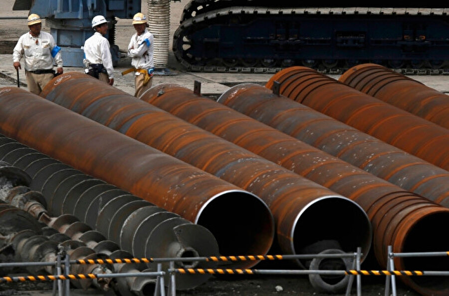 Tokyo'daki bir inşaat sahasında çeliklerin yanında duran işçiler.