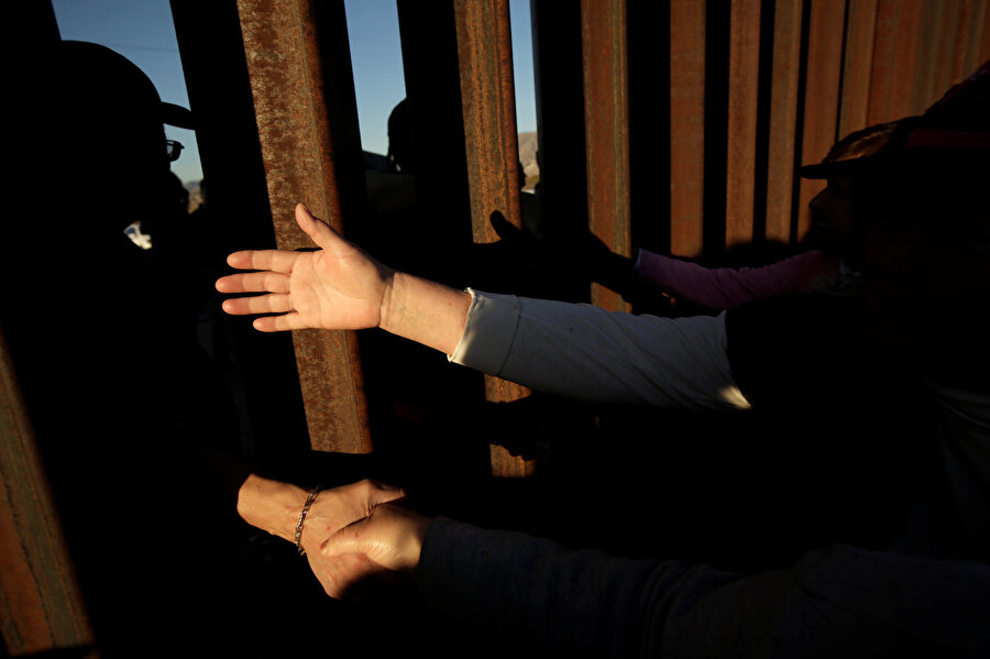 Meksika ve ABD arasındaki sınır tellerinin her iki tarafında duran insanlar. 