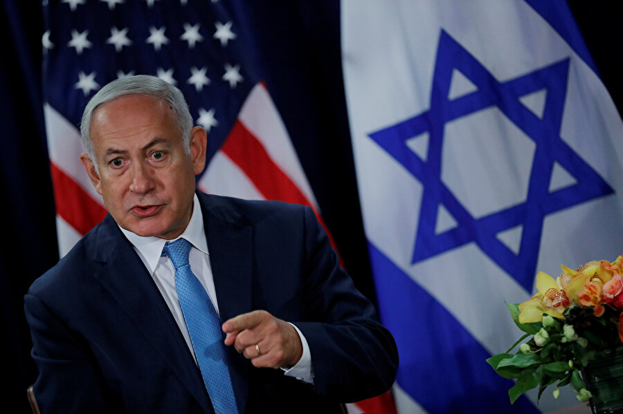İsrail Başbakanı Binyamin Netanyahu ABD ve İsrail bayraklarının önünde görünüyor.