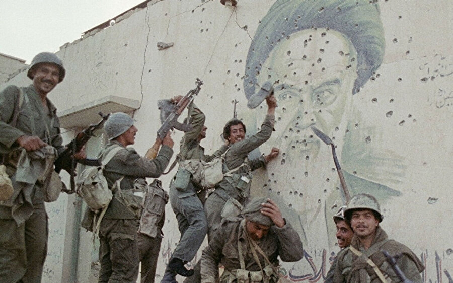 Irak askerleri, İran’lı lider Ayetullah Humeynî’nin kurşun izleriyle kapanan duvardaki resminin önünde poz veriyor, 20 Nisan 1988.