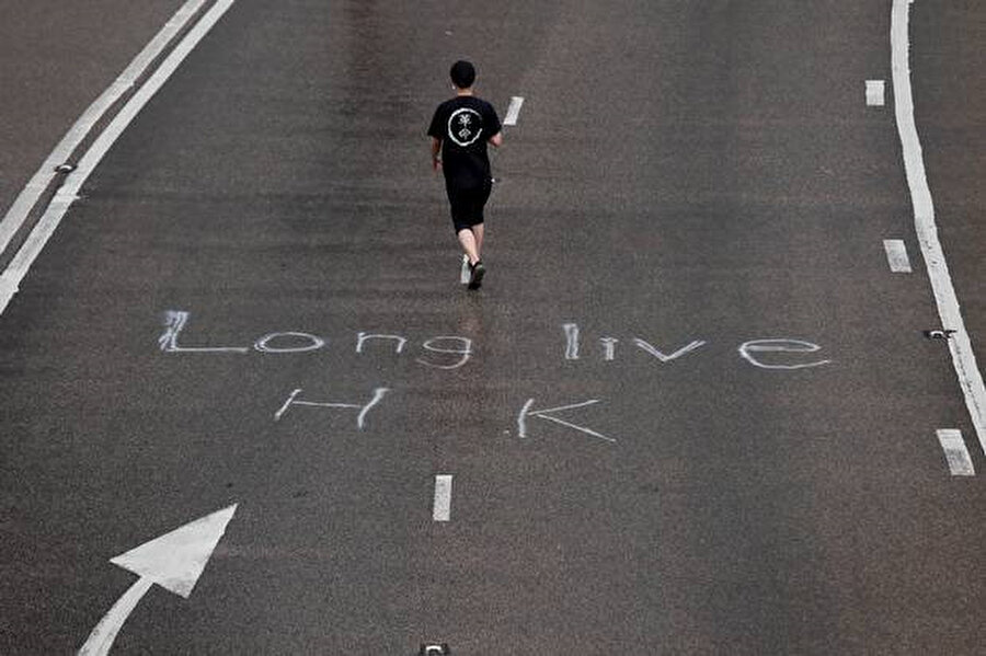  Bir protestocu yolda boyanmış Long Live Hong Kong (Çok yaşa) kelimelerinin olduğu caddede yürüyor. 