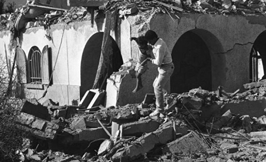 1 Ekim 1985'te İsrail uçaklarının, FKÖ'ye ait Hammam Şat Karargahını bombalamasının ardından kurtarma ekibine mensup bir görevli enkazın arasından bir çocuğu çıkarıyor.