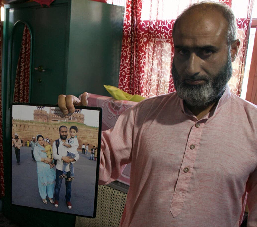 Rafiq Shagoo, göz yaşartıcı gazın evinin içine dolması sonucu hayatını kaybeden eşi Fehmeeda Bano ve oğullarının olduğu aile fotoğraflarını gösteriyor. (Zubair Sofi/The Independent)
