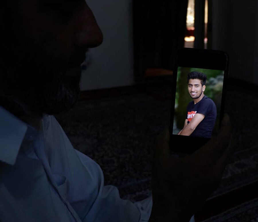 Polisten kaçmak için nehre atladıktan sonra yaşamını yitiren 17 yaşındaki Osain Altaf'ın babası Ahmad Marazi, oğlunun ekrandaki görüntüsüyle teselli olmaya çalışıyor. ( Zubair Sofi/The Independent)