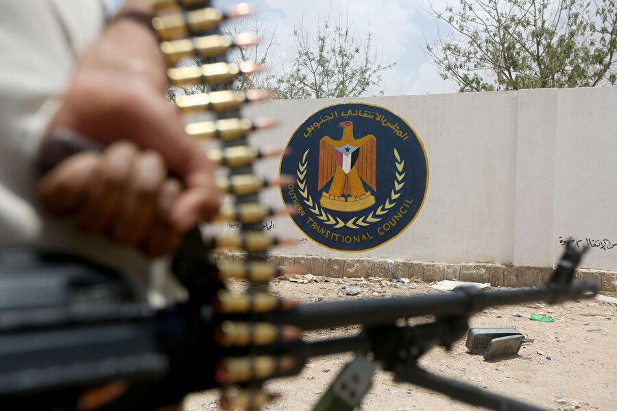 Yemen hükümetine bağlı bir asker, Güney Geçiş Konseyi merkezine yakın bir noktada amblemin önünde silahıyla poz veriyor.