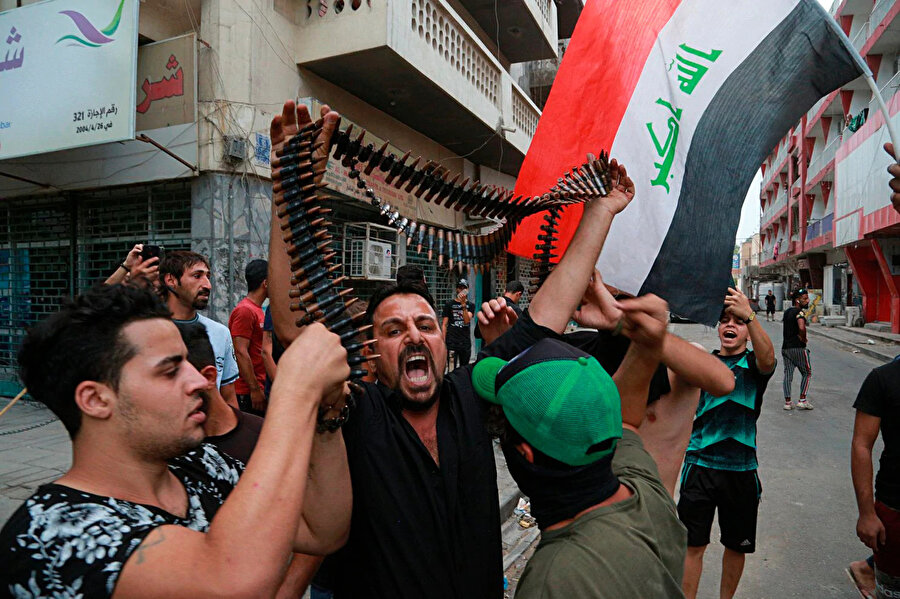 Göstericiler Irak polisinden aldıkları kurşunları havaya kaldırırken görülüyor.