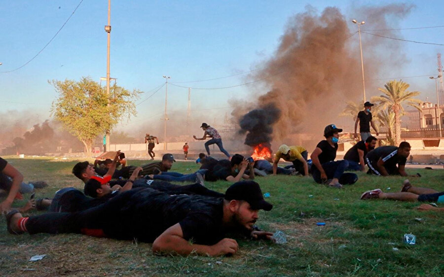 Irak polisinin açtığı ateş karşısında siper alan göstericiler.