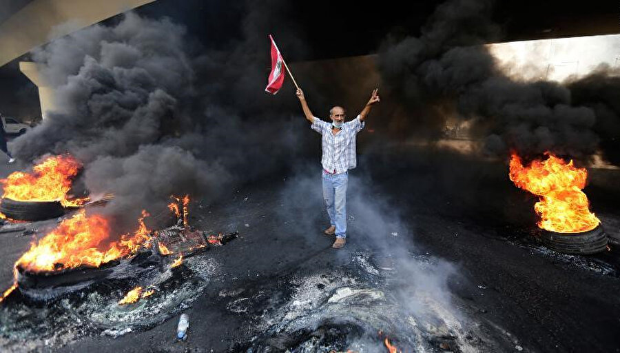 Elinde Lübnan bayrağı bulunan protestocu bir eliyle de zafer işareti yapıyor.
